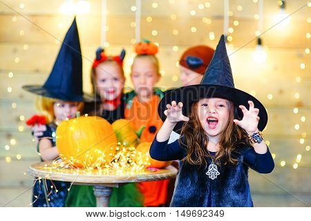 Happy group of witch children pirate and demons during Halloween party playing around the table with pumpkins