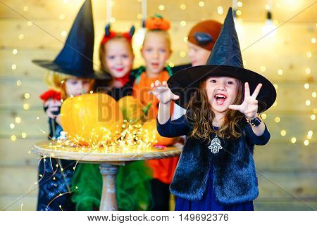 Happy group of witch children pirate and demons during Halloween party playing around the table with pumpkins