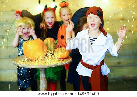 Happy group of witch children pirate and demons during Halloween party playing around the table with pumpkins