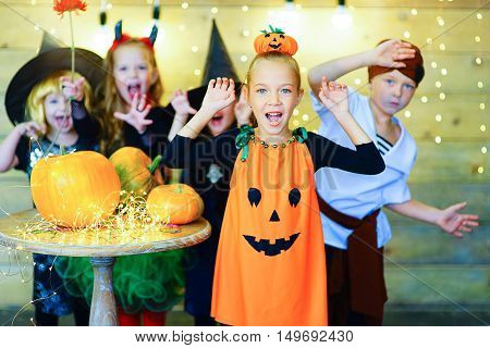 Happy group of witch children pirate and demons during Halloween party playing around the table with pumpkins