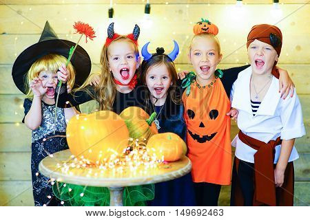 Happy group of witch children pirate and demons during Halloween party playing around the table with pumpkins