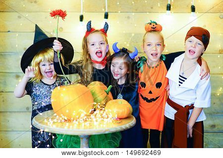 Happy group of witch children pirate and demons during Halloween party playing around the table with pumpkins