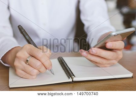 Woman hands using smartphone and writing on notebook