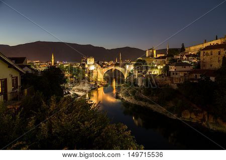 A view of the Mostar skyline at night towards the Old Bridge (Stari Most). Buildings and the River Neretva can be seen.
