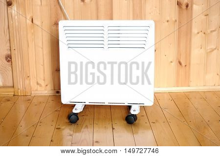 Working white electric convector heater plugged to power line in a wooden house room front view closeup