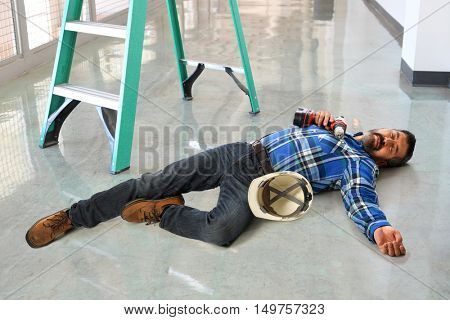 Hispanic worker laying injured on floor next to ladder