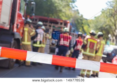 Team of blured firefighters by firetruck on protected accident site. Focus on red and white security band.