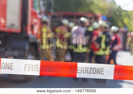 Team of blured firefighters by firetruck on protected accident site. Focus on red and white security band.
