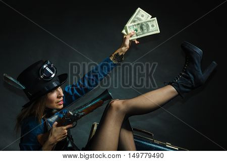 Fashionable subculture weapon concept. Steampunk girl with cash. Young gorgeous lady in victorian fashion lying on floor with banknotes briefcase and blunderbuss.