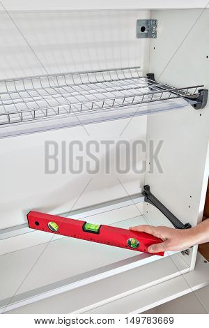 Installation of kitchen furniture assembling of shelving plate rack handyman measuring the level with special tool close-up of craftsperson hands holding red spirit level.
