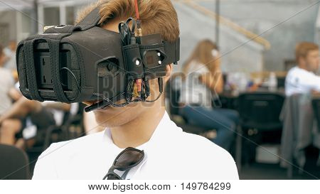 Back view of man watching flight of FPV drone using Virtual Reality glasses. Drone control training process in sunny day. Quadrocopter competitions outdoors.