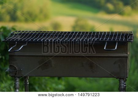 a empty portable BBQ grill in front of a fresh green summer landscape