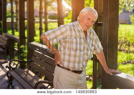 Senior man has backache. Elderly male outdoors. Disease of spine. Strong pains during movement.
