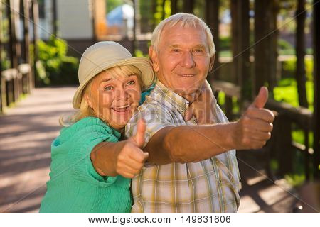 Elderly woman hugging man. Senior couple showing thumbs up. Loving hearts don't get tired. Many years spent together.