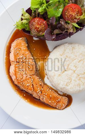 Fusion food style grilled salmon dressed with Japanese sweet sauce (Teriyaki) including Thai rice garnished with vegetables in ceramic dish