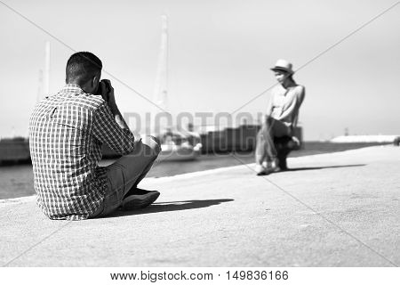 Young photographer taking picture of his girlfriend in seaport with boat in background - Man shooting girl outdoor in summertime - Black and white editing - Retro glamour concept - Vintage raw filter