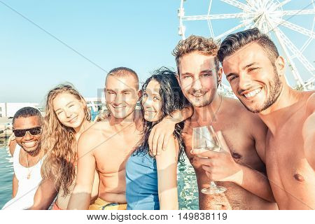 Group of multiracial friends having fun in boat summer party - Young people taking selfie photo with ferris wheel in background - Happiness and friendship concept - Warm vintage filter