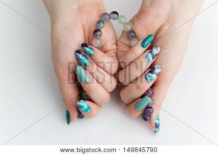 Closeup of woman nails with creative purple and green manicure. Fluorinit print. Natural stone beads. Copy space.