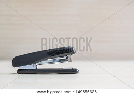 Closeup black stapler office equipment on blurred wood desk and wall in office room textured background under window light