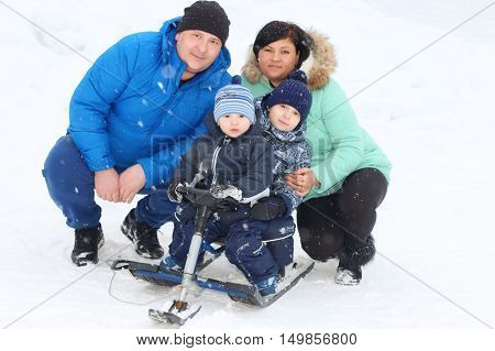 Happy family (father mother two sons) pose with snowracer during snowfall in winter day
