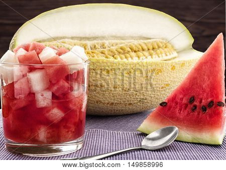 The cut pieces of melon and watermelon juice in a glass on blue napkin