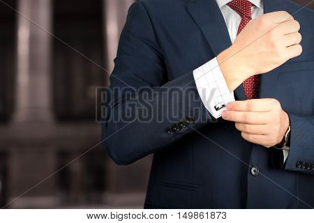 business and office concept - elegant young fashion buisness man in a blue/navy suit touching at his cufflinks