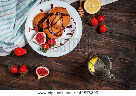 A cup of tea and pancakes with figs strawberries on white plate closeup.