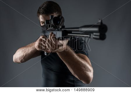man in black military uniform aiming with rifle isolated on gray close-up