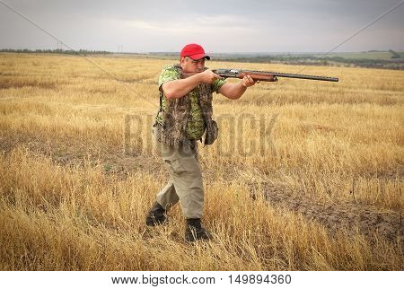 Hunter with a gun on the field aiming at the prey