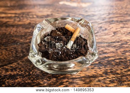 Cigarette butts with ash in ashtray on wooden table