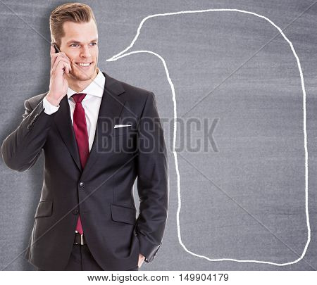 Businessman Talking On The Phone In Front Of A Blackboard With Large Speech Bubble..