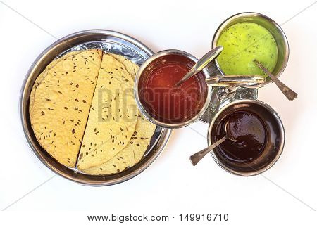 Indian bread served with the traditional assortment of sauces, in the typical tableware. Shot from above on white background