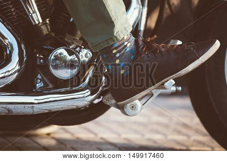Close-up of foot in polka dot sock and leather shoe on throttle pedal of bike