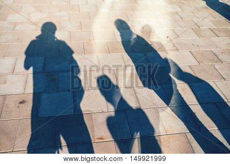 People casting shadows on the pavement four young man and women overshadowing street concrete tiles