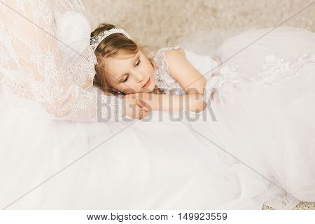 Littel princess lies on her mother in white dress.