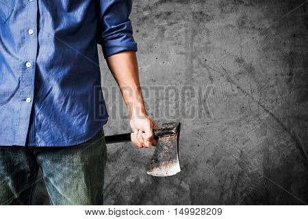 A guy holding old rusty axe, close up front view, on dark concrete texture background with copy space
