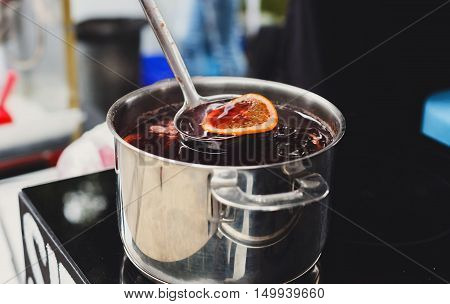 Making mulled wine for sale at country fair. Glintwine with citrus and cloves in big metal stock pot, mixed with soup ladle. Fall and winter warming beverage