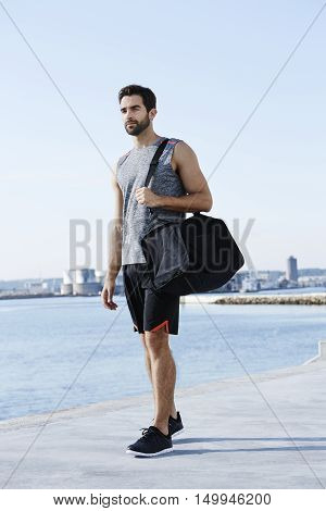 Cool athlete with sports bag walking near the sea