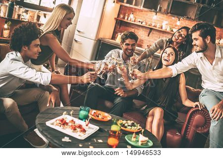 Cheers to best friends! Group of cheerful young people enjoying food and drinks while spending nice time in cofortable chairs on the kitchen together