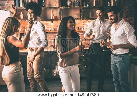 Friends enjoying party . Cheerful young people dancing and drinking while enjoying home party on the kitchen