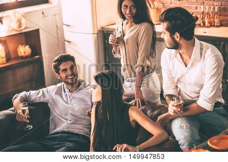 Friends will be friends. Cheerful young people enjoying food and drinks while spending nice time in cofortable chairs at home together