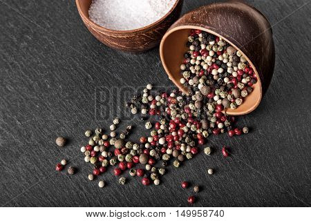 salt and pepper in a clay bowl on a slate board spices are scattered