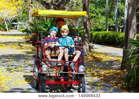 Yound dad and two little kid boys biking on bicycle in zoo. Family with active leisure and watching animals. Father and sons having fun together.