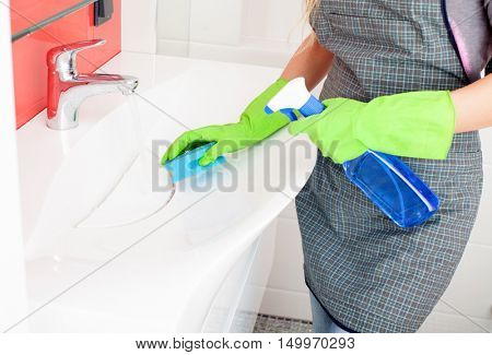 Woman cleaning sink and faucet in bathroom at home