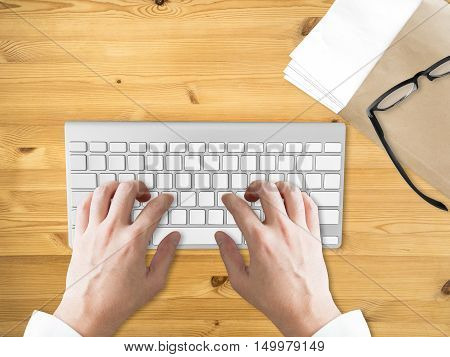 Working on computer with folder of document and eyeglasses.
