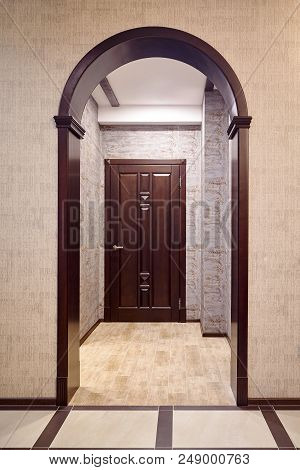 Passage Through Wooden Archway Into Corridor With Entrance Door Tiked In Brown Tones Example Of Mode