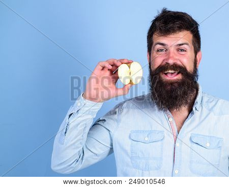 Man Bearded Smiling Holds Apple Blue Background. Half Of Apple Healthy Lifestyle. Hipster Demonstrat