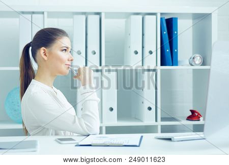Pensive Young Business Woman Sitting Turning Sideways At The Dask With Desktop Monitor And Looking A