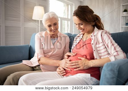 Beaming Woman. Beaming Smiling Woman Feeling Extremely Happy While Touching Pregnant Tummy Of Her Da