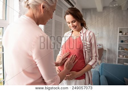 Hands On Tummy. Excited Mother Putting Her Hands On Pregnant Tummy Of Her Daughter While Visiting He